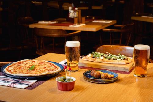 a table with two pizzas and two glasses of beer at Sheraton Skyline Hotel London Heathrow in Hillingdon