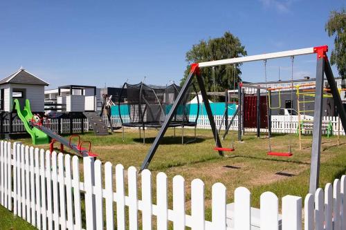 a playground with swings and a white fence at Przyczepa Coco Camp z klimatyzacją w Molo Surf in Jastarnia