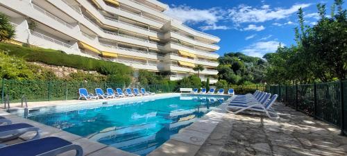 une piscine avec des chaises bleues et un bâtiment dans l'établissement Cannes - Sea View- Swimming Pool - Parking - Beach, à Cannes