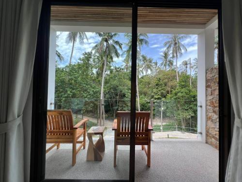 two chairs and a table on a patio with palm trees at Woodlawn Villas Resort in Koh Tao