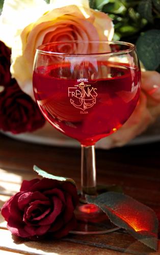 a glass of red wine sitting on a table with a rose at Frank's Hotel in Capoliveri