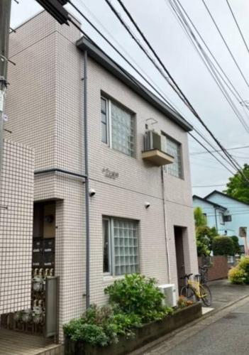a white brick house with a balcony on a street at 完全プライベートルーム 東京 府中駅徒歩圏内 高速フリーWifi キッチン洗濯機完備 二人でも宿泊可 in Fuchu