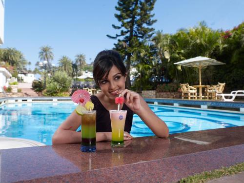 a woman sitting at a table with two cocktails at Hotel Hillock in Mount Ābu