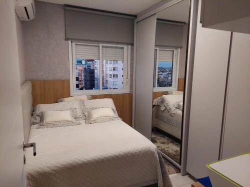 ein kleines Schlafzimmer mit einem Bett und zwei Fenstern in der Unterkunft Belo Apartamento no Centro de Capão da Canoa in Capão da Canoa