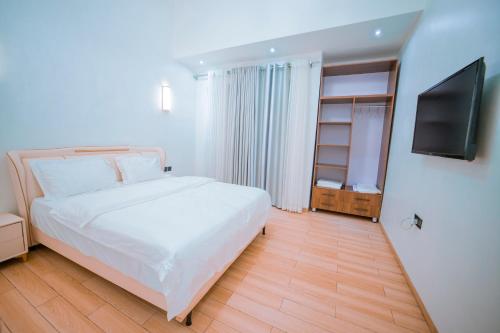 une chambre avec un lit blanc et une télévision à écran plat dans l'établissement The Milon Apartment, à Kigali