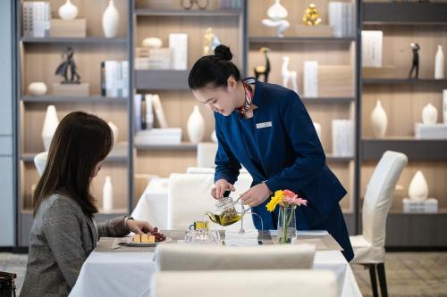 a woman standing in front of a table preparing food at Mehood Lestie International Hotel Linhexi Guangzhou East Railway Station Branch - Free Shuttle Bus to Canton Fair Complex During Canton Fair Period & Free afternoon tea & Free midnight snack & Free VPN Internet Access in Guangzhou