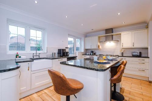 a kitchen with white cabinets and a island with bar stools at Kinship House by YourStays - Stunning Holiday Home in the Suburbs in Newcastle under Lyme