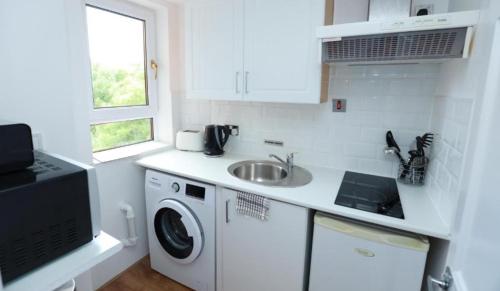 a white kitchen with a sink and a washing machine at Glasgow South Studio in Glasgow