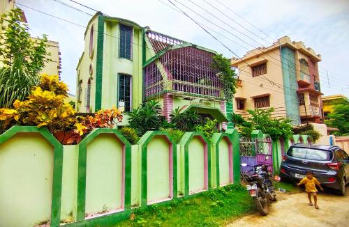 a green and white building with a fence with flowers at Alor Niloy in Purulia
