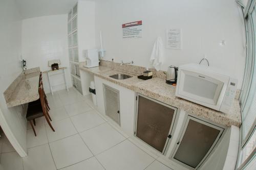 a white kitchen with a sink and a microwave at Hotel Dinamarca in Balneário Camboriú