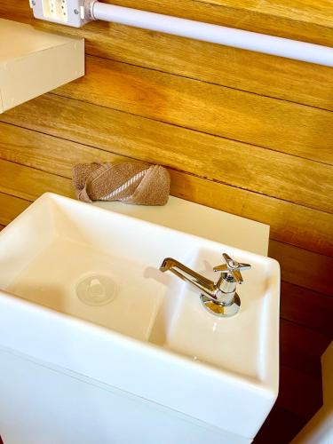 a white sink in a bathroom next to a wooden wall at Chalé Barril com cozinha in São Francisco do Sul