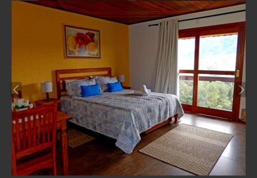 a bedroom with a bed with blue pillows and a window at Pousada do Sonho, PARTE ALTA in Visconde De Maua