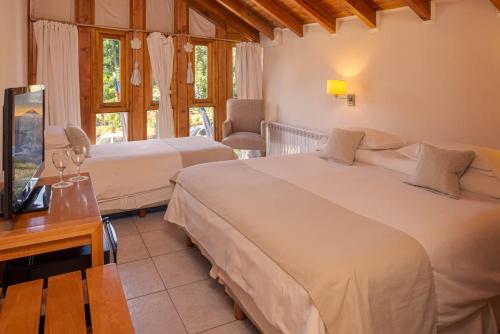 a bedroom with two beds and a desk with a television at Hotel Antiguos in San Martín de los Andes