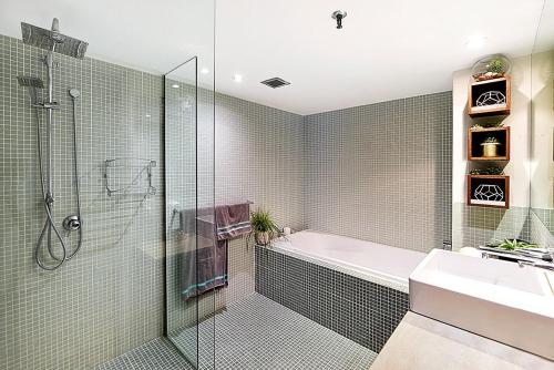 a bathroom with a shower and a tub and a sink at Absolute Beachfront Apartment 3B Pool Spa in Gold Coast
