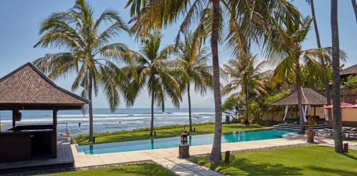 a resort with a pool and palm trees and the ocean at Pushpapuri Villa in Ketewel