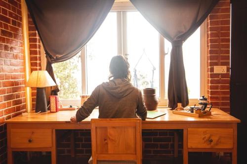 a woman sitting at a desk looking out a window at Les Terrasses Himalayan Resort in Charikot