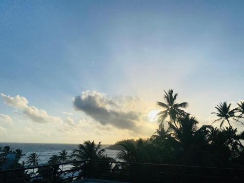 a view of the ocean with palm trees and the sunset at The Wave's Guest House in Mirissa