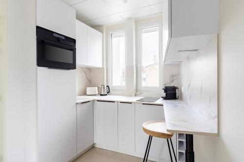 a white kitchen with white cabinets and a stool at Appart Hôtel Résidence Courcelle in Levallois-Perret