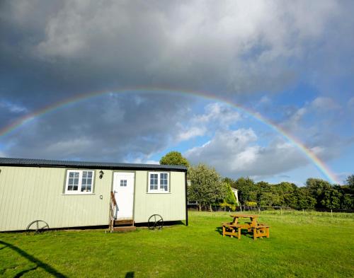 a rainbow over a building and a picnic table at Cwtch Glamping Shepherds Huts in Abergavenny