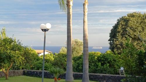 two palm trees and a street light with a cruise ship in the ocean at Profumo di Zagara Acireale in Acireale