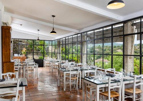 un restaurant avec des tables et des chaises blanches et de grandes fenêtres dans l'établissement Hôtel Restaurant Les Remparts, à Venasque