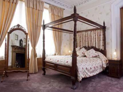 ein Schlafzimmer mit einem Himmelbett und einem Kamin in der Unterkunft The Royal Hotel Tain in Tain
