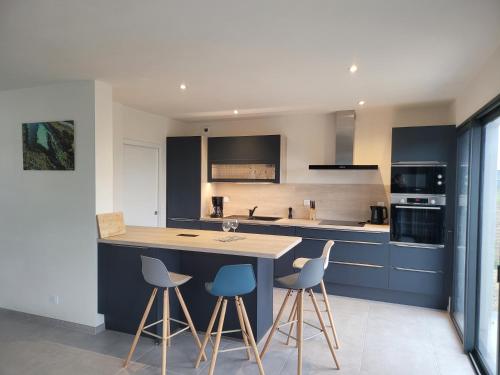 a kitchen with blue cabinets and a table and stools at Villa l'estran récente vue mer Plounéour-Brignogan-plages in Plounéour-Trez