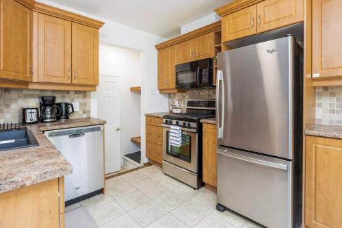 a kitchen with wooden cabinets and a stainless steel refrigerator at Cozy Modern 4BR Home with Sunny Patio in Ottawa