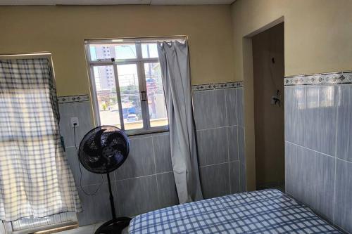 a room with a bed and a window and a fan at Kitnet alojamento independente in Nova Iguaçu