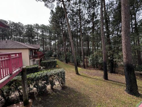 a house with a red porch in a forest at Appartement Spacieux rénové et piscine chauffée 1Chambre 4 personnes - Lacanau - piscine - Vue sur le golf in Lacanau