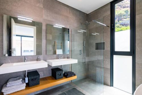 Un baño con dos lavabos y una ducha de cristal. en CasaMar, en Jardim do Mar