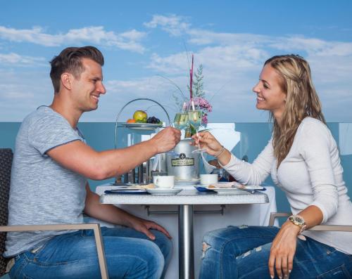 a man and a woman sitting at a table with a drink at Joglland Hotel Prettenhofer in Wenigzell