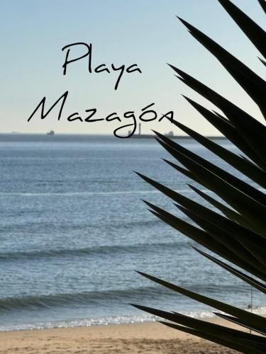 a view of the ocean from a beach with a palm tree at Casa Mazagón con vistas al mar in Mazagón