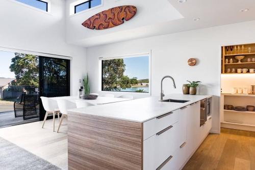 a kitchen with white cabinets and a large window at Wainui Townhouses, Two Modern, Waterfront Units in Raglan