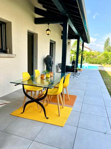 a glass table and yellow chairs on a patio at Villa des cèdres in Saint-Bonnet-les-Oules