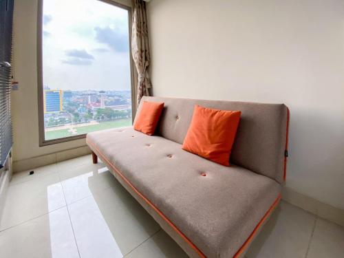 a couch with two orange pillows in a room with a window at Good Deal Studio Apartment at Warhol (W/R) Residences By Travelio in Semarang