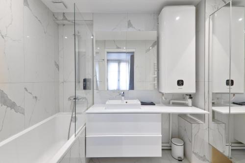 La salle de bains blanche est pourvue d'un lavabo, d'une baignoire et d'un miroir. dans l'établissement Appartement Quartier Rue de la Paix Free Netflix, à Paris