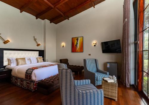 a bedroom with a bed and two chairs and a tv at Gorilla Heights Lodge by NEWMARK in Kisoro