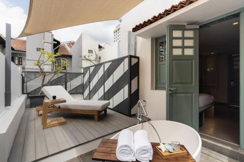 a room with a balcony with a tub and a chair at Claude Hotel in Singapore