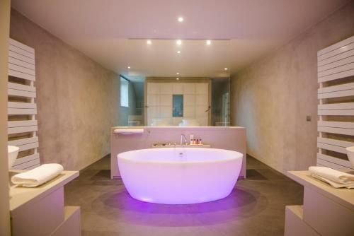 La salle de bains est pourvue d'une grande baignoire blanche et d'un lavabo. dans l'établissement Ne5t Hotel & Spa, à Namur