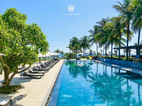 a large swimming pool with chairs and palm trees at The Ocean Villas Managed by The Ocean Resort in Da Nang