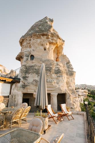 a patio with an umbrella and chairs and a stone building at Paradise Cappadocia Hotel & Rooftop in Göreme