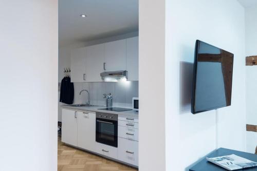 a kitchen with white cabinets and a tv on a wall at HITrental Chapel Bridge Apartments in Luzern