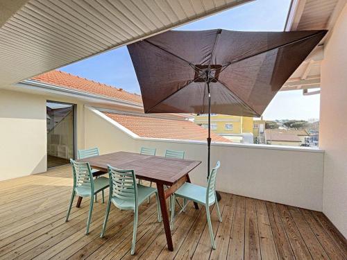 d'une table en bois avec des chaises et un parasol sur le balcon. dans l'établissement Agréable 3 chambres extra centre à 200m de l'océan, à Biscarrosse