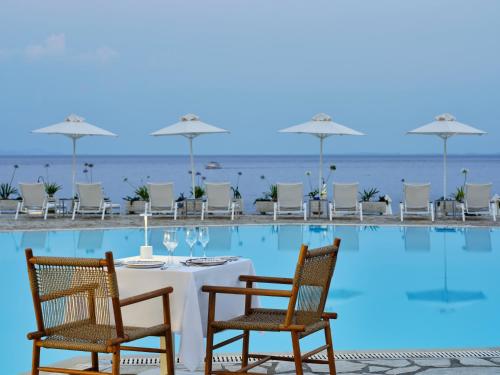 a table with wine glasses and chairs next to a pool at Atlantica Nissaki Beach - Adults Only in Gimari