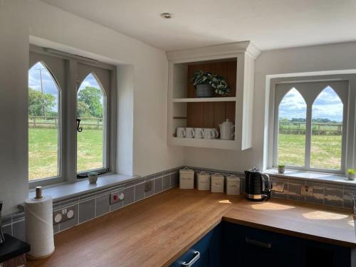 eine Küche mit drei Fenstern und einer Holzarbeitsplatte in der Unterkunft Old Cottage - English Countryside Retreat in Lindsell