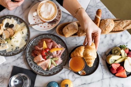 a table with plates of food and a person reaching for a piece of bread at Casinohotel Velden in Velden am Wörthersee