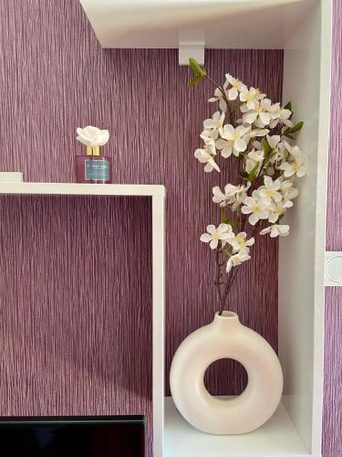 a white vase with white flowers in a room at City view & pool apartment 2 in Niš