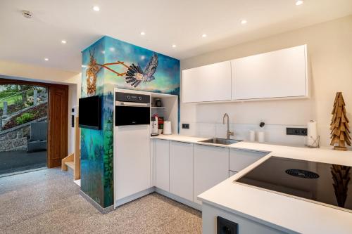 a kitchen with white cabinets and a peacock painting on the wall at Waldlux Luxus-Chalet Brennhus in Kappelrodeck