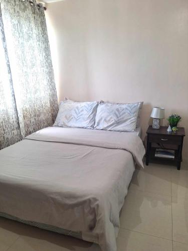 Una cama en un dormitorio con ventana y mesita de noche. en AJ Condominium, en Cebú